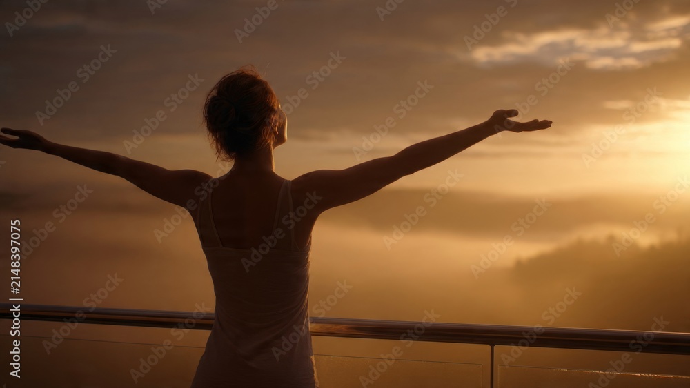Fototapeta premium A young woman practicing mindfulness welcomes a new day with open arms on her balcony at sunrise enveloped in soft golden light and a peaceful morning ambiance