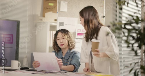 Asian female graphic designers brainstorm design ideas at studio desk. Two business woman working together on branding project over a visual layout. creative marketing, teamwork, coordination concept.