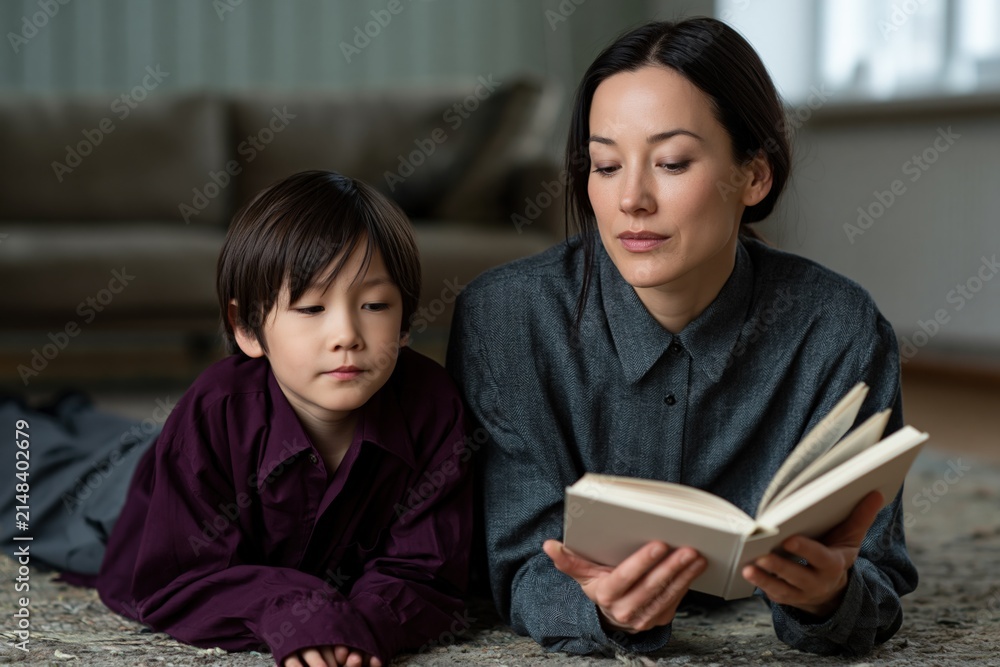Obraz premium Mother and child reading a book together on the floor for cozy family reading background and home education banner design