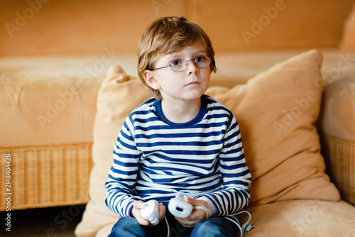 Cuadro en lienzo Cute little blond kid boy with glasses playing with a video game console
