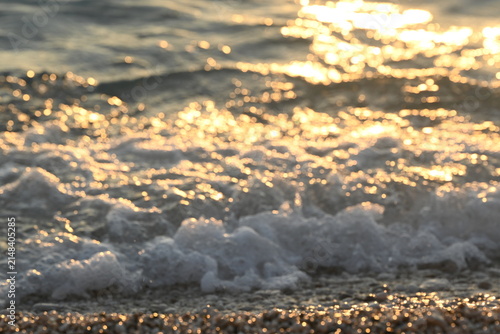 Title: Golden sunlight reflecting on shimmering ocean surface and soft sea foam on beach close up abstract background