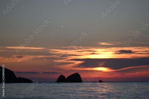  Beautiful golden sunset over the sea with rock silhouettes and copy space in the sky. Romantic summer evening background from Lefkada island, Greece.