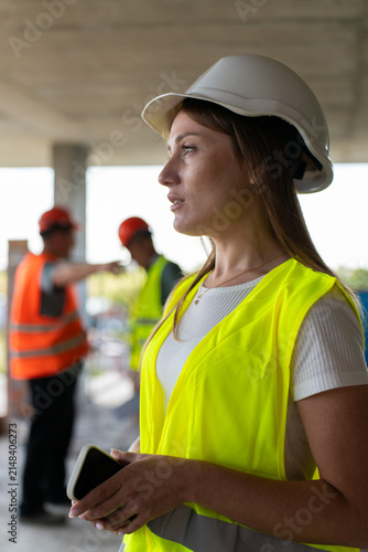Cuadro en lienzo Inspector in hard hat stands in profile with phone near hand on site