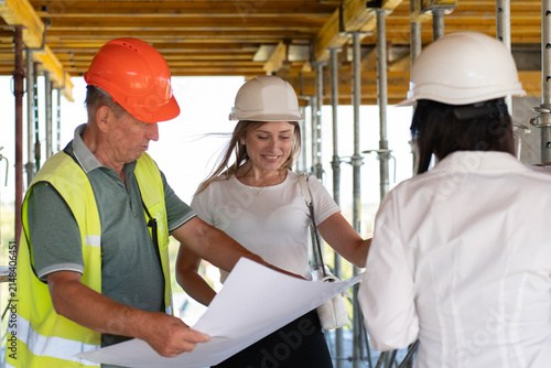 Construction engineers review blueprints working together at building site. Inspectors and foreman discuss plan at unfinished structure