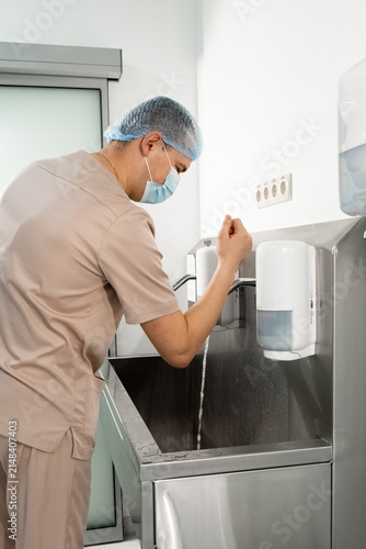 Healthcare specialist washes hands before with running water sterile medical work in clinic. Infection prevention hygiene routine vertical shot