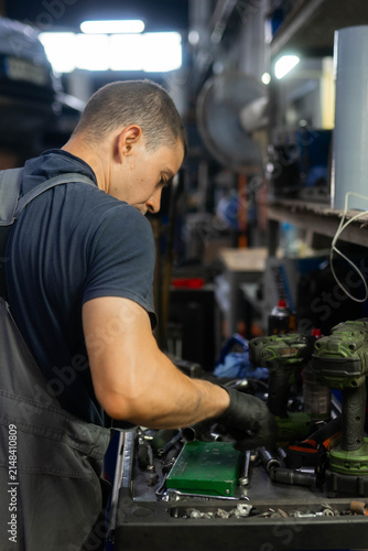 Young mechanic takes spanner for car repair at service station vertical shot. Technician chooses instruments on workbench in workshop