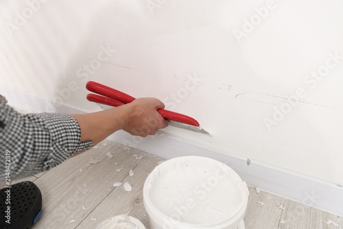 Worker plastering white wall with putty knife indoors, closeup