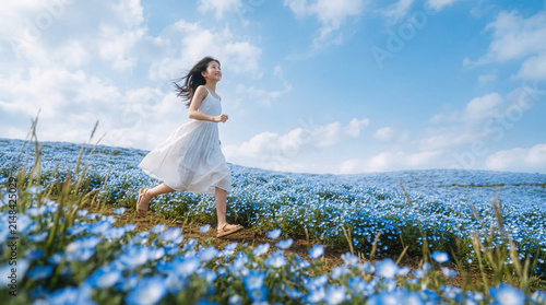 Joyful young woman running through a nemophila flower field under blue sky