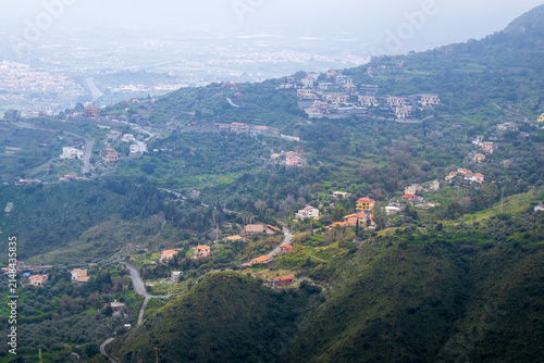 Fotografía Wide landscape of hilly terrain covered with opuntia cactus stretches beneath mountainside village near Castelmola