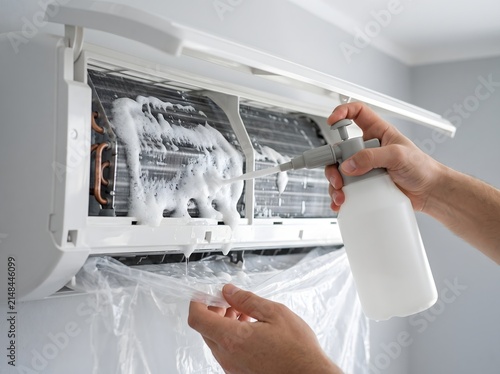Professional technician cleaning a residential air conditioner unit with foam spray cleaner.