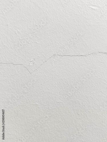 Фотография A textured white painted concrete wall showing a fine hairline crack, suitable as a minimalist architectural background or backdrop