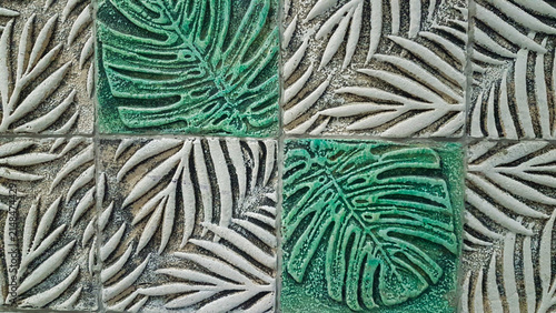 Full frame texture of decorative ceramic wall tiles featuring embossed tropical monstera and palm leaf motifs in vibrant green and white shades.
