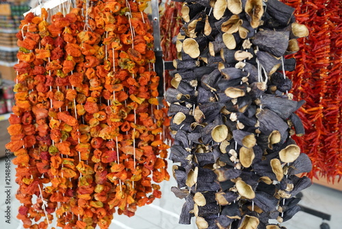 Colorful dried peppers and eggplants hanging in strings at a traditional market, showcasing natural food preservation, vibrant textures and authentic ingredients for regional cuisine.