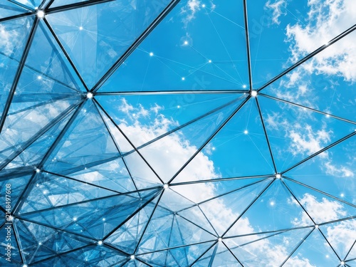 Modern Geometric Architecture: The intricate geometric design of a modern building's glass facade reflects a clear blue sky with fluffy clouds.