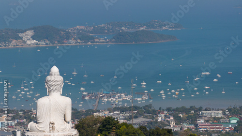 Aerial view of the Big Buddha Phuket overlooking the bay filled with numerous boats and yachts, with lush green hills and coastal urban development in Karon, Phuket, Thailand.