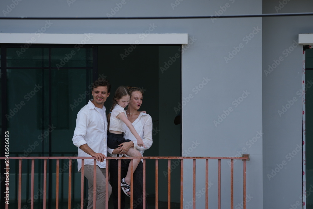 Obraz premium Young parents holding their child greet the neighborhood from the balcony with their daughter on the balcony of their new house overlooking the residential estate