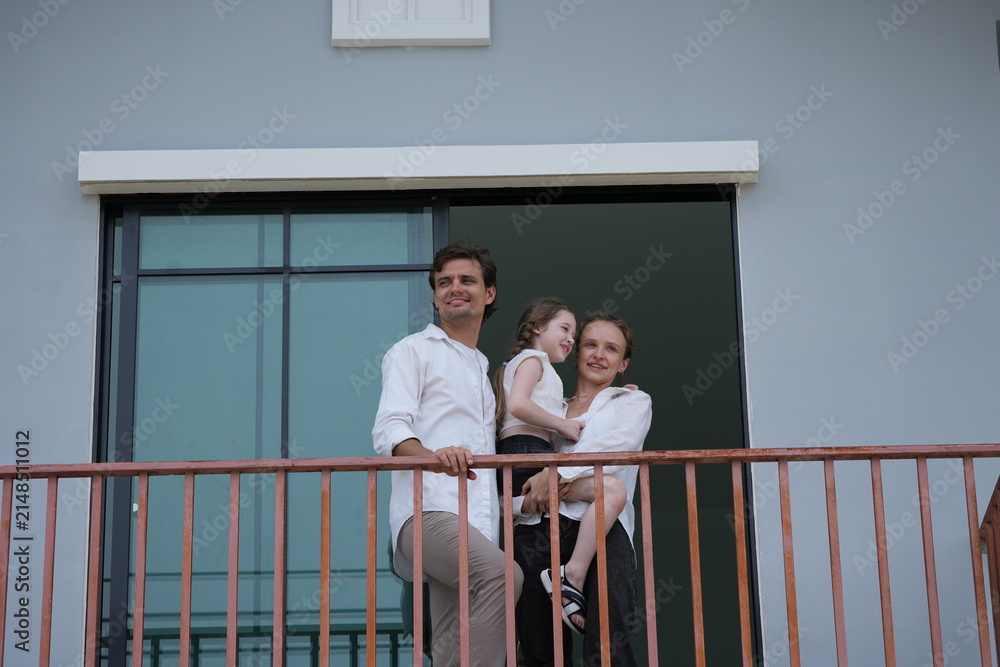 Obraz premium Happy young family with little daughter greet the neighborhood from the balcony with their daughter on the upper balcony of their new home above the neighborhood, shallow depth of field