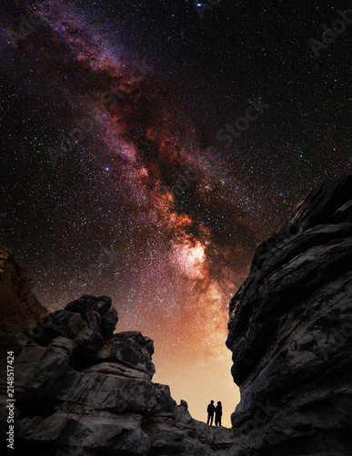 Night landscape. Lovers silhouette stands on the rock and looks at Milky Way galaxy.