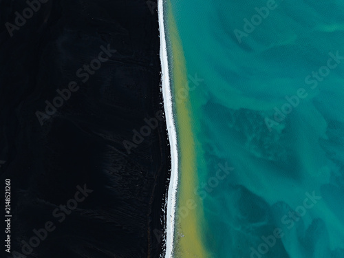 Aerial view of a black sand beach meeting turquoise glacial water in Iceland.