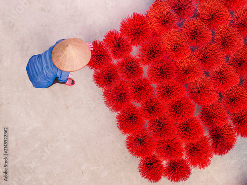 Aerial view of a person in a conical hat arranging vibrant red incense bundles on a concrete surface in Vietnam.