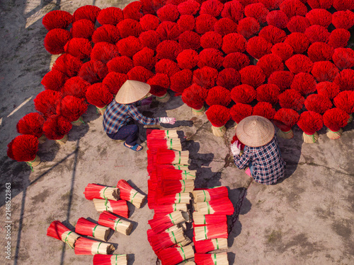 Aerial view of workers wearing traditional conical hats while drying bright red incense sticks on the ground in Vietnam.