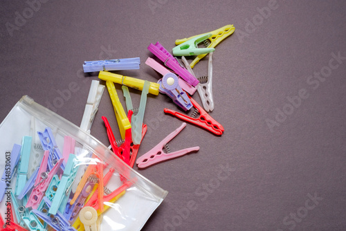 Fotografie Colorful plastic clothes pegs spilling from bag on dark surface