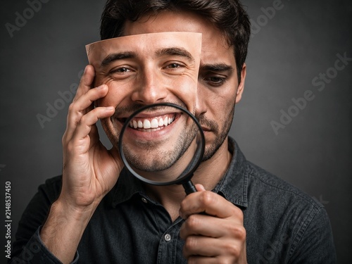 Man holding smiling mask while looking serious with magnifying glass  