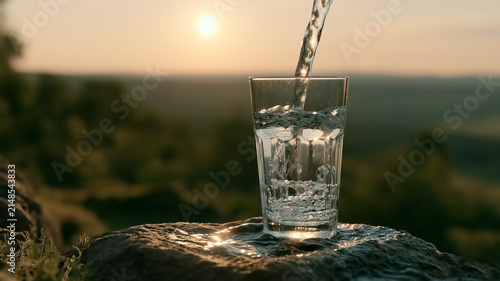 Fresh Water Pouring into Clear Glass at Sunset on Wet Rock, Refreshing Hydration Concept in Golden Light. Global Warming, Global Warming and Water Conservation Concept. Copy Space,  Aspect 16:9