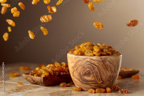 Obraz na plátně Yellow sultana raisins pour into a wooden bowl.