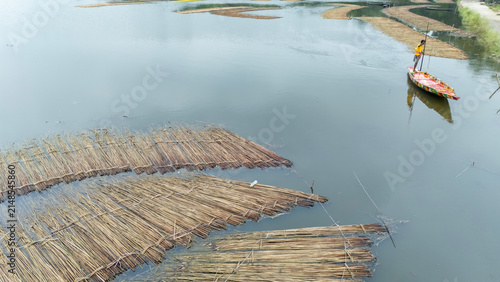 A man rows a small wooden boat across the monsoon-flooded waters of Bortir Bil, North 24 Parganas, West Bengal, India. This seasonal wetland, known for jute harvesting and red water lilies.