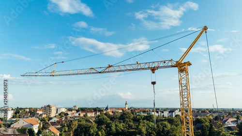 Aerial view of a yellow construction crane towering over the urban landscape with residential buildings and lush green trees in Sremska Mitrovica, Vojvodina, Serbia.