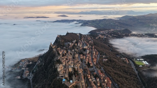 Aerial view of the historic city of San Marino perched on Mount Titano above a sea of clouds during golden hour in San Marino, San Marino, San Marino.