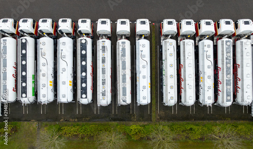 Wognum, Noord-Holland, Netherlands - 27 April 2024: Aerial view of a fleet of white tanker trucks parked in neat rows at a logistics facility.