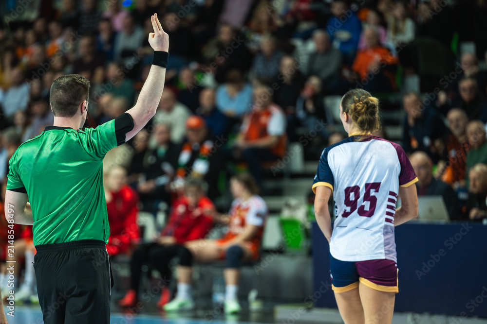 Fototapeta premium A handball referee showing a two-minute suspension sign with fingers during a high-stakes professional sports game.