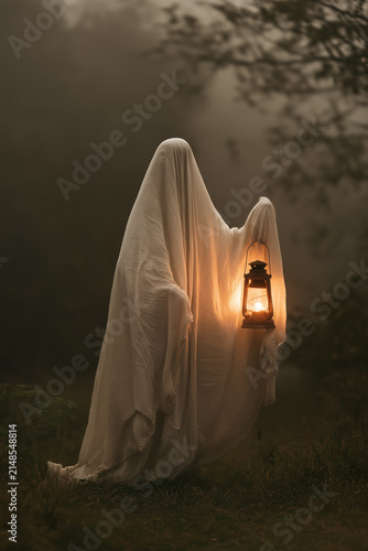 Ghostly Figure Holding Vintage Lantern in Misty Woodland with Warm Light and Haunting Ethereal Foggy Atmosphere. Copy Space, vertical aspect 2:3.
