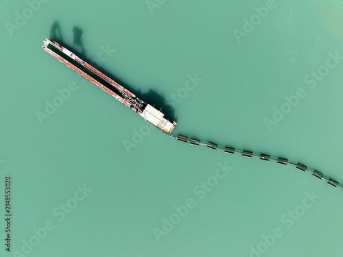 Aerial view of a long industrial barge with a floating containment boom trailing behind on the turquoise water of the Mondego River in Coimbra, Coimbra District, Portugal.