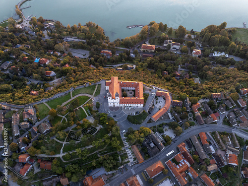 Aerial view of Tihany Abbey surrounded by lush greenery, historic rooftops, and the scenic Lake Balaton in Tihany, Hungary.