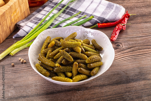 фотографія Pickled gherkins in white bowl with green onions and red chili peppers on wooden