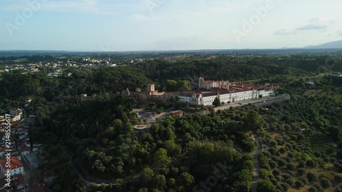 Aerial view of the historic Convent of Christ in Tomar surrounded by lush green forests and rolling hills in Portugal.