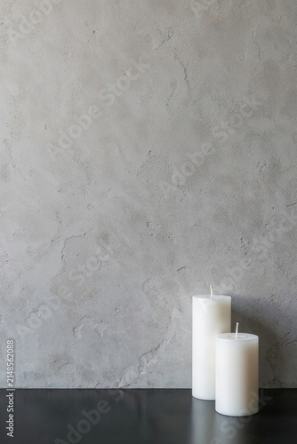 Two white unlit pillar candles on a dark table surface