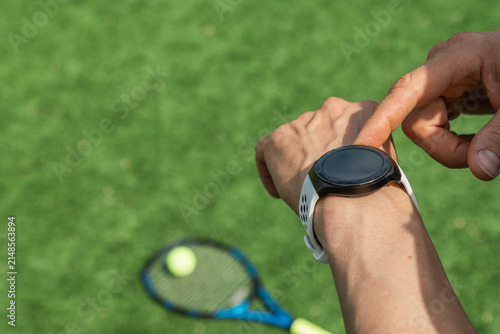 Caucasian athlete checking smartwatch before tennis practice on outdoor court. Fitness tracking wearable technology and active healthy lifestyle with copy space.
