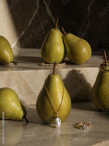 Luxury still life photography with fresh green pears and elegant gold jewelry featuring pearls and diamonds on marble surface for high end cosmetic brand promotion