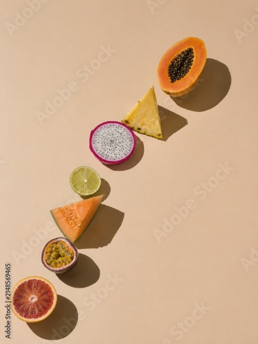 Minimalist flat lay composition of exotic tropical fruit halves arranged diagonally casting sharp shadows on warm beige background for summer branding design