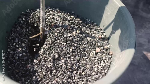 A close-up of dark gravel being mixed in a gray plastic bucket with a construction mixer. The gravel is mixed with a special solution for laying decorative paths. Preparing gravel for laying landscape