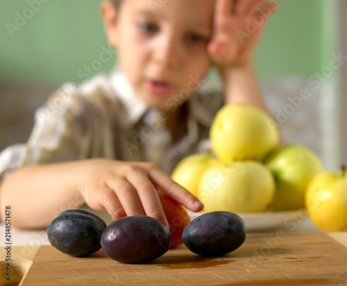 boy's hand reaching for a fresh natural plum among organic fruit on a wooden board