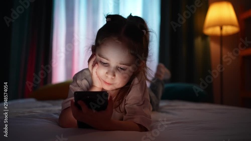 Close-up of a child using a smartphone in a room in the evening.