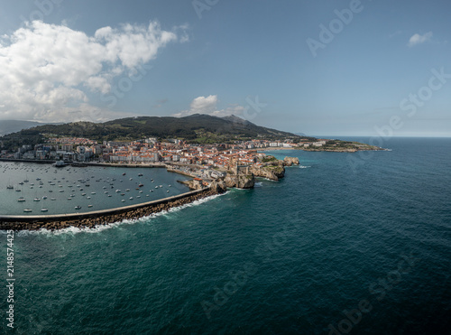 Aerial view of the coastal town of Castro Urdiales featuring its historic lighthouse, harbor filled with boats, and breakwater extending into the sea in Castro Urdiales, Cantabria, Spain.
