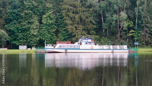 Boat floats on a calm lake surrounded by trees during a sunny afternoon