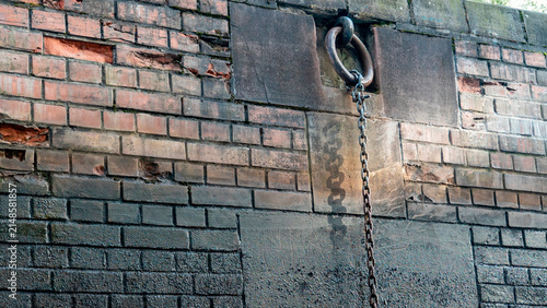 Old metal ring and chain attached to a brick wall in an abandoned location during daytime