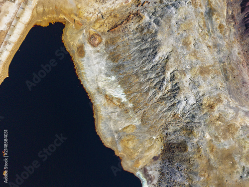Aerial view of the mining landscape at Achada do Gamo featuring a dark acidic water reservoir and rugged terrain with mineral deposits in Achada do Gamo, Beja, Portugal.